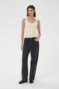 Top tank beige a costine con pizzo, abbinato a jeans scuri grigio a vita alta e larghi. Modello con scarpe nere. Sfondo minimalista.