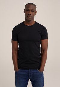 Camiseta negra de manga corta en una tela elástica, con cuello redondo y un corte ajustado. Combinada con jeans de mezclilla azules. Diseño y textura simples.