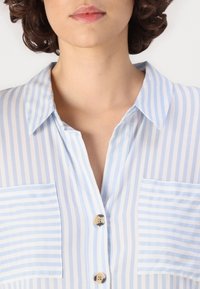 Lightweight, button-up shirt in light blue and white vertical stripes; features two chest pockets and collar. Smooth, sheer fabric.