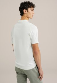 Polo alb cu mânecă scurtă, cu accente texturate pe umeri, guler și tiv ribbed. Material neted, cu un design ajustat.