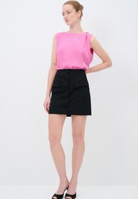 Roze mouwloze top met een zachte textuur en een bootnek, gecombineerd met een zwarte mini-jurk met knopen aan de voorkant en zijzakken.