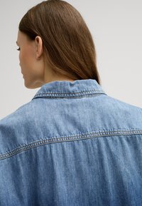 Light blue denim jacket with a classic collar, visible stitching, and a relaxed fit, showcasing a soft texture and subtle sheen.