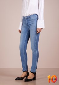 Slim fit jeans i ljusblå denim, med medelhög midja och vit sidrand. Kombineras med svarta klackskor med blockhäl och en vit blus.