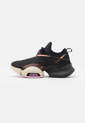 Chaussure de sport noire et or rose avec tige en mesh, coussin d'air visible dans la semelle, languette à l'arrière et fermeture à lacets, vue de profil.