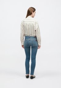 Camisola de mangas compridas às riscas em cores claras; jeans azuis justos; sapatilhas pretas; vista de costas. Textura lisa e design ajustado.