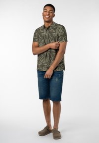 Grünes kurzärmliges Hemd mit Blättermuster, kombiniert mit blauen Denim-Shorts und grauen Slippern. Lässiges Outfit-Design mit lockerer Passform.