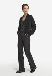 Svart kort cardigan med ribbat mönster, matchad med en svart tanktop och högmidjade svarta byxor. Blanka svarta skor fulländar looken.