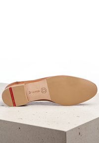 Suela de zapato de cuero con un acabado suave y color beige claro. Presenta un acento rojo y una marca en relieve. Patrón texturizado cerca del talón para mayor agarre.