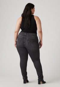 Donkergrijze skinny jeans met een aansluitend ontwerp, voorzien van twee achterzakken, subtiele stiksels en een hoge tailleband; gecombineerd met een zwart tanktop.