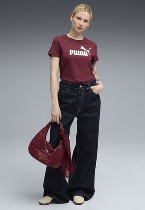 Tricou din bumbac burgundy cu logo-ul alb "PUMA", asortat cu blugi negri din denim cu talie înaltă și picior larg, și o geantă maroon cu o eșarfă cu model.