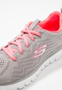 Graue Sport-Sneaker mit einem strukturierten Mesh-Obermaterial, leuchtend pinken Schnürsenkeln und Innenfutter. Verfügt über eine weiße gepolsterte Sohle und Logo-Akzent.
