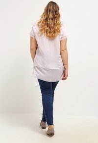 Lyser�ød bluse med korte ærmer, løs pasform og en buet kant, parret med mørkeblå smalle jeans og brune ankelstøvler.