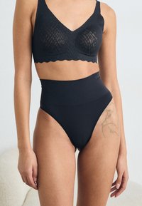 Black, high-waisted underwear with smooth texture and a seamless design. The bra features a scalloped edge and a patterned overlay.