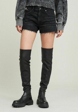 Zwarte denim shorts met een gefranjerde zoom, gecombineerd met zwarte leren laarzen tot boven de dij met een chunky zool en een zijkant rits. Gelaagd, robuust uiterlijk.