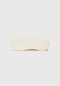 Weißer Gummisohlen mit strukturierter Oberfläche, geprägt mit Branding, runder Zehenform und zurückhaltenden Designelementen.