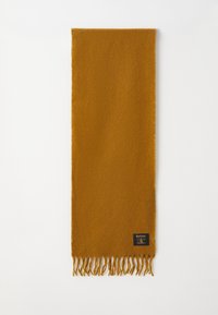 Mustard-yellow scarf made of soft material, featuring fringed edges and a small brand label on one end. Rectangular shape, simple design.
