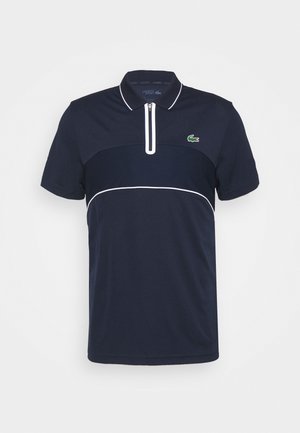 Granatowa koszulka polo z krótkim rękawem, przednim białym zamkiem, białym przeszyciem i zielonym logo krokodyla Lacoste na piersi.