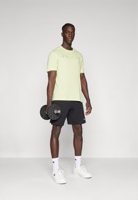 Light green short-sleeve Champion t-shirt, black shorts, holding dumbbells. White sneakers and matching socks with logo featured.