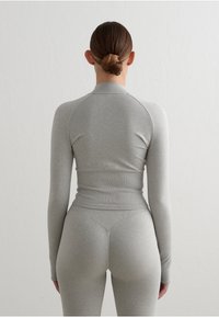 Camiseta atlética de manga larga gris y leggings a juego, hechos de una tela elástica, con un diseño ajustado y textura acanalada.