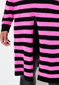 Neulemekko, jossa on vaakasuoria mustia ja vaaleanpunaisia raidallisia kuvioita, pitkät hihat, ribbireunat ja sivussa olan helpottamiseksi.