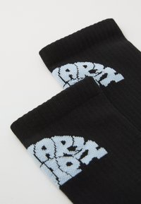 Chaussettes noires avec une texture côtelée présentant un graphique "ARMEE" en bleu clair imprimé dans une police audacieuse et déformée près du bord.