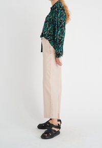 Blusa nera a fiori con dettagli verdi, pantaloni beige a gamba larga e sandali neri con cinturini. Tessuto strutturato con una vestibilità rilassata.