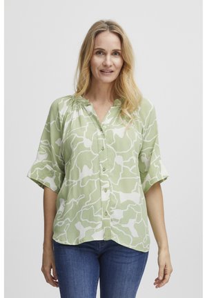 Camisa de botón verde claro con patrón abstracto blanco, con mangas cortas enrolladas y un corte relajado, fabricada con un tejido ligero.