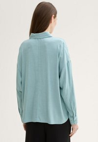 Camisa de manga larga azul claro en una suave tela texturada, con yugo trasero, cuello y puños abotonados. Silueta simple y relajada.