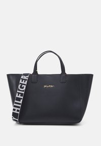 Sac tote en cuir noir avec double poignées, bandoulière en tissu de marque amovible et logo Tommy Hilfiger en métal doré à l'avant.
