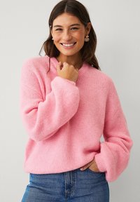 Maglione rosa in morbido maglione a maglia con vestibilità rilassata, texture a coste e maniche larghe, abbinato a jeans di denim blu.