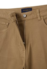 Pantalones de algodón en color beige con cremallera y cierre de botón. Incluye una etiqueta con "PIOMBO" y bolsillos laterales. Tela texturizada visible.