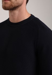 Marineblauer strukturierter Pullover mit einem gerippten Rundhalsausschnitt und Rautenmuster, der dezente kontrastierende Paneeldetails auf den Schultern aufweist.