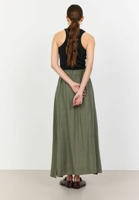 Top senza maniche nera abbinata a una lunga gonna verde oliva con cintura elastica e spacco laterale. La modella indossa delle scarpe piatte marroni.