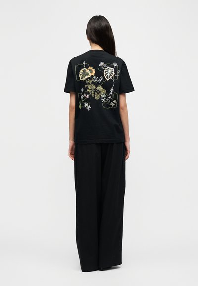 Μαύρο βαμβακερό μπλουζάκι με πολύχρωμη κεντητική με λουλούδια στην πλάτη. Άνετη γραμμή με κοντά μανίκια, συνδυασμένο με φαρδιά μαύρα παντελόνια.