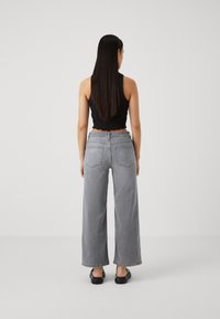 Svart ärmlös topp och grå högmidjade vida jeans; jeansen har två bakfickor och en rak passform; mjuk denimtextur.