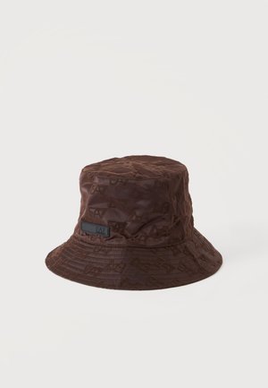 Brun bucket hat med diskrete præget mønstre og en lille sort rektangulær label foran mod en ensartet lys baggrund.