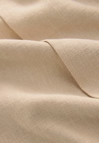 Béžová tkanina s viditeľnou textúrou tkania, jemnými záhybmi a miernymi tieňmi zvýrazňujúcimi jej prírodný ľanový materiál.