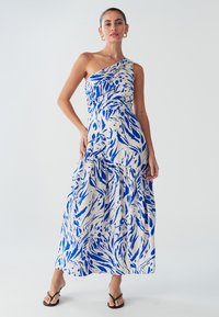 Robe longue asymétrique blanche avec motifs abstraits bleus, doté de fronces à la taille et d'une jupe fluide, confectionnée en tissu léger.