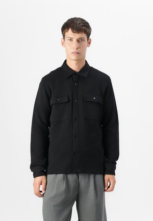 Black long-sleeve button-up shirt with two chest pockets, crafted from textured fabric, featuring a collared neck and front button closure.