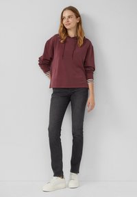 Hoodie bordeaux avec un cordon de serrage, poignets rayés, associé à un jean noir et des sneakers blanches. Tissu doux et coupe décontractée.