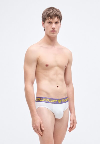 Λευκά ανδρικά εσώρουχα με διακοσμητική μωβ μέση που διαθέτει χρυσό σχεδιασμό με ρόλο. Το ύφασμα φαίνεται λείο και εφαρμοστό στο σώμα.