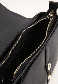 Inre i svart tygväska med flera fack. Metalliska guldfärgad dragkedjor och hårdvara. Slät textur med en strukturerad form.