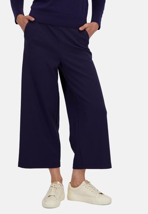 Pantalons larges bleu marine en matière douce, avec une taille haute et des poches latérales, associés à des baskets blanches pour un look décontracté.
