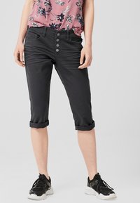 Pantalons courts noirs en tissu extensible, dotés d'une fermeture à boutons avec trois boutons. Manches retroussées et texture lisse. Associés à des baskets sombres.