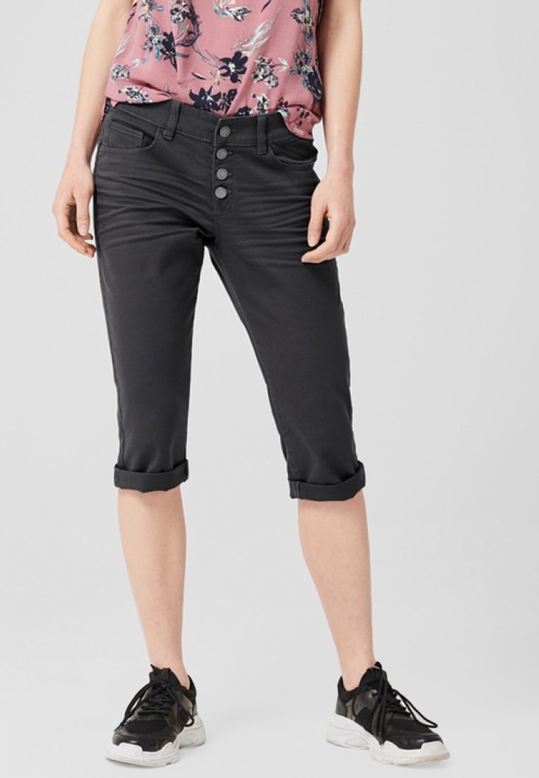 Pantalons courts noirs en tissu extensible, dotés d'une fermeture à boutons avec trois boutons. Manches retroussées et texture lisse. Associés à des baskets sombres.