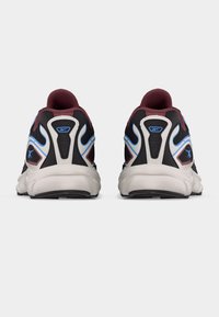 Ζευγάρι αθλητικών παπουτσιών σε μαύρο, λευκό, μπλε και βυσσινί, εμφανιζόμενα από πίσω με παχιά λευκά πέλματα και εμφανή λογότυπα της μάρκας.