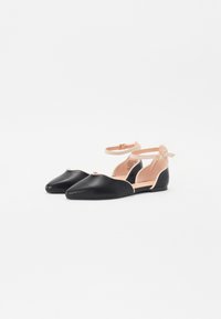 Ballerine nere in pelle con punta appuntita, dotate di un cinturino alla caviglia color nude e una texture liscia. Il design presenta dettagli con bordo scallop.