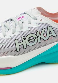 Bežecká obuv má svetlosivú sieťovanú vrchnú časť s výrazným logom "HOKA", teal medzipodrážku a štruktúrované akcenty v bielej a ružovej farbe.