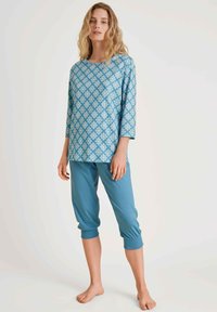 Lichtblauw pyjama set met een gestreepte lange mouwen top en een cropped broek. De top heeft een geometrisch patroon; de broek is effen blauw.