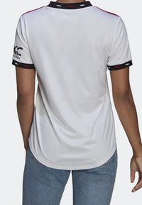 Camiseta deportiva blanca con un acabado texturizado, que presenta detalles en negro y rojo en el cuello y las mangas, diseñada con un corte relajado.